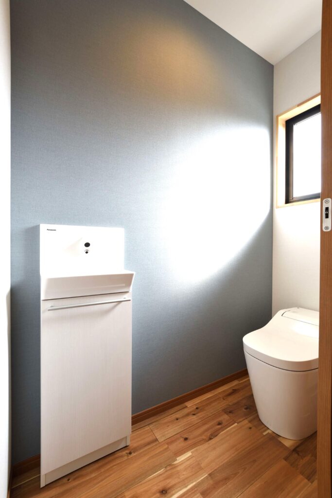 落ち着いた色味のアクセントクロスが印象的なトイレ空間。小窓からは自然光が差し込んでいる。