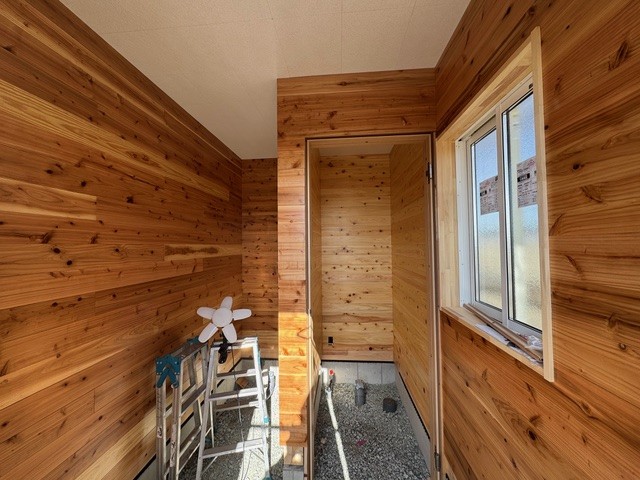 室内の壁一面に木板を張った内装下地。個室の間仕切りと窓を備えた明るい空間