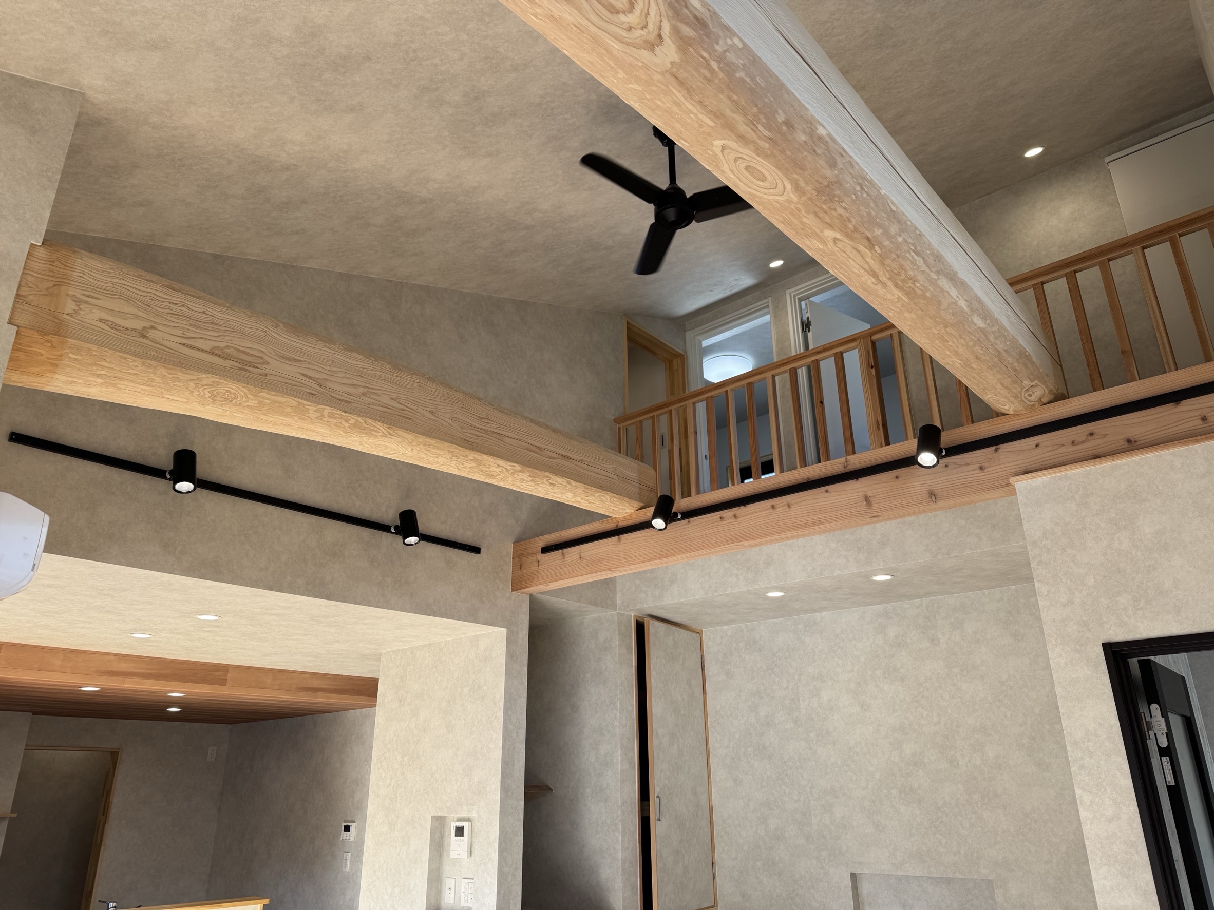 吹き抜け上部に大きな梁が架かる室内写真｜上下階がつながる開放的な新築住宅