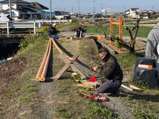 地面に座り、鯉のぼりの先端に取り付ける矢車や回転球などの細かい部品を丁寧に組み立てる様子。